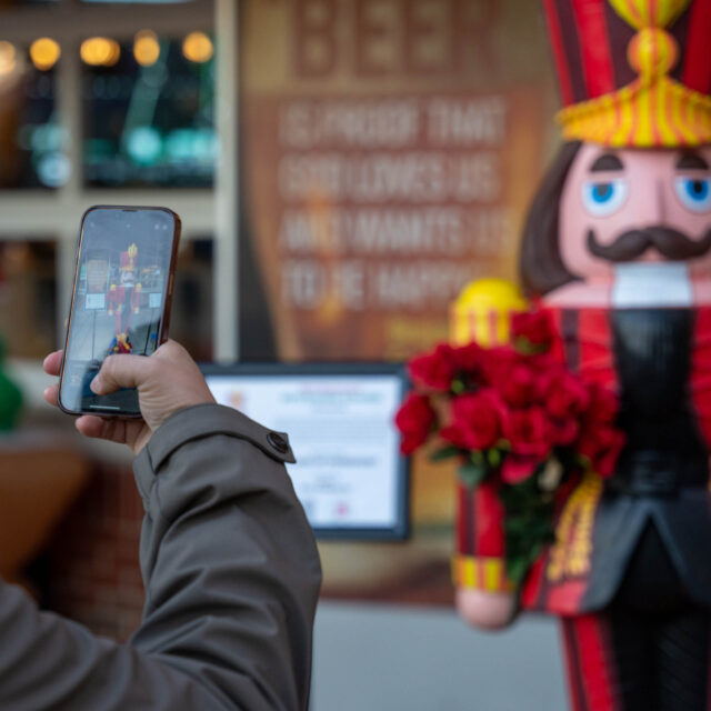 Person taking a photo of a large decorative nutcracker figure holding roses with their smartphone in a festive setting.