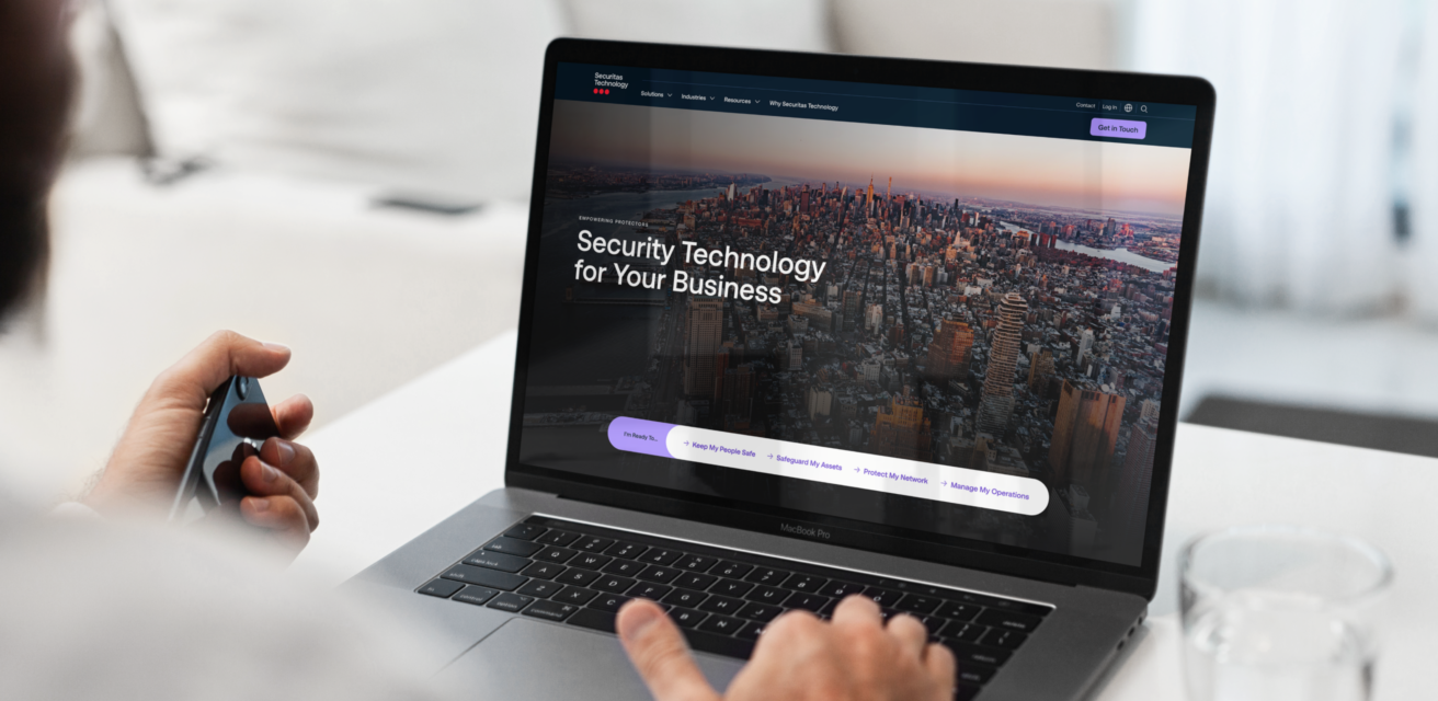 A person is using a laptop displaying a website with a cityscape image and the text "Security Technology for Your Business.